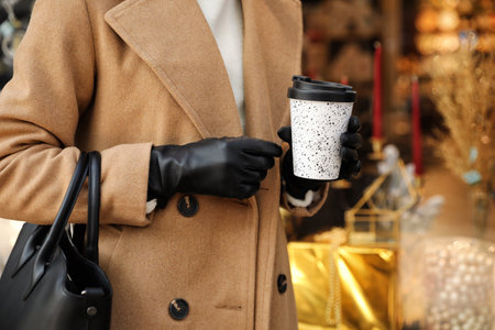Woman with stylish leather gloves and cup of coffee near store decorated for Christmas, closeupの写真素材