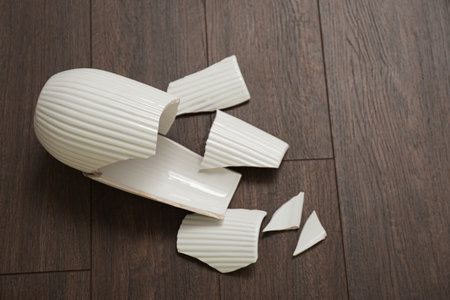 Broken white ceramic vase on wooden floor, above view