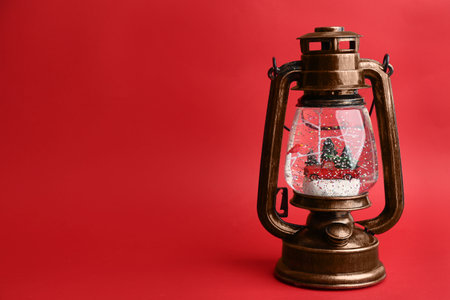 Beautiful snow globe in vintage lantern on red background, space for textの写真素材