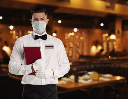 Waiter in medical face mask in restaurant. Space for textの写真素材