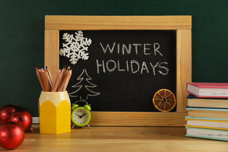Chalkboard with text Winter Holidays, Christmas decor and school supplies on wooden tableの写真素材