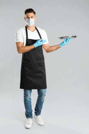 Waiter in medical face mask with empty tray on light gray backgroundの写真素材