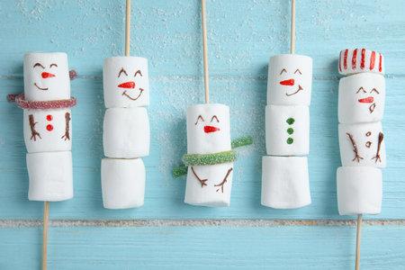Cute snowmen made of marshmallows on light blue wooden background, flat layの写真素材