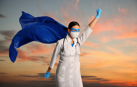 Medical workers fighting dangerous diseases. Doctor dressed as superhero posing against skyの写真素材