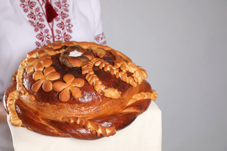 Woman holding korovai on gray background, closeup with space for text. Ukrainian bread and salt...