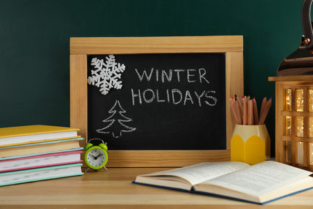 Chalkboard with text Winter Holidays and school supplies on wooden tableの写真素材