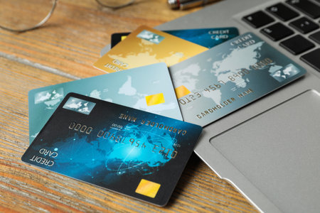 Different credit cards near laptop on wooden table