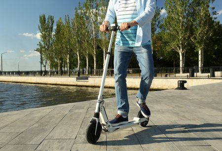 Man riding modern kick scooter along waterfront, closeup
