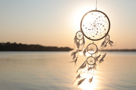 Beautiful handmade dream catcher near the river at sunset. Space for textの写真素材