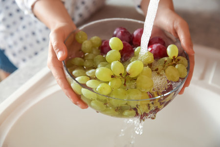 Woman washing fresh grapes in kitchen sink, closeupの写真素材