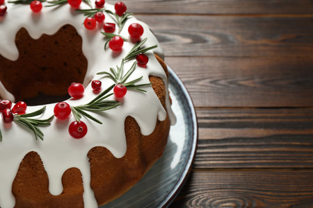 Traditional Christmas cake decorated with glaze, pomegranate seeds, cranberries and rosemary on wooden table, closeup. Space for textの写真素材