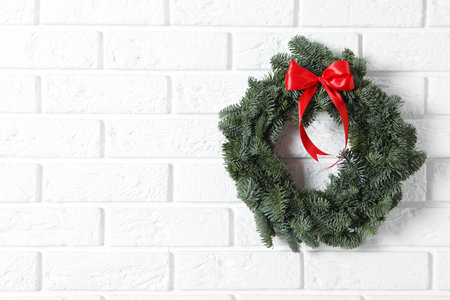 Christmas wreath made of fir tree branches with red ribbon on white brick wall, space for textの写真素材