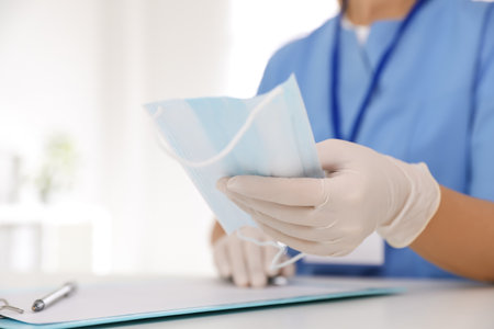 Doctor in medical gloves holding protective mask at table in office, closeupの写真素材