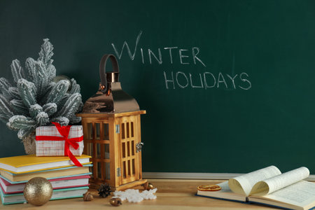 Text Winter Holidays on chalkboard near wooden table with Christmas decor and booksの写真素材