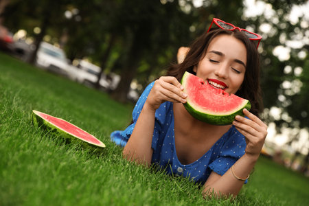 Beautiful young woman with watermelon in park on sunny dayの写真素材