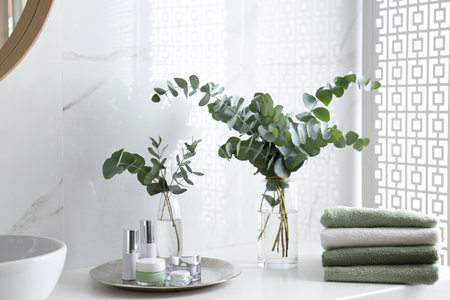 Fresh eucalyptus branches and cosmetic products on countertop in bathroomの写真素材