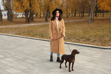 Woman in protective mask with German Shorthaired Pointer in park.