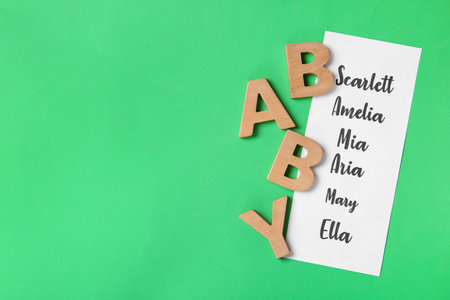 List of baby names and wooden letters on green background, flat lay. Space for textの写真素材