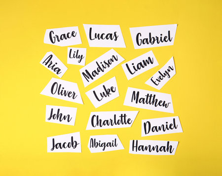 Paper sheets with written different baby names on yellow background, flat layの写真素材