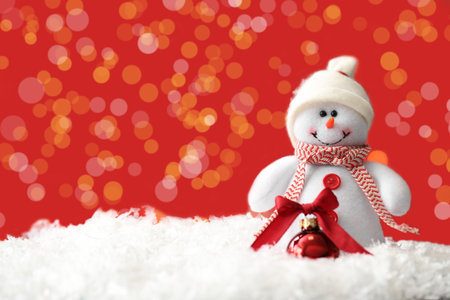 Snowman toy and Christmas ball on snow against blurred festive lights. Space for textの写真素材