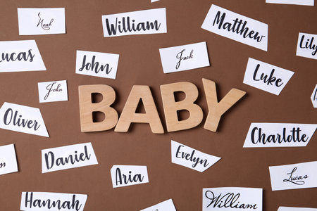 Paper sheets with written different baby names and wooden letters on brown background, flat layの写真素材