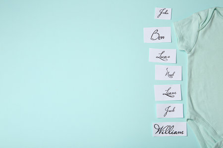 Paper sheets with written different baby names and bodysuit on light blue background, flat lay. Space for textの写真素材