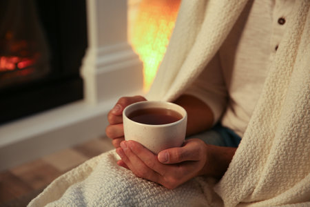 Man covered with white plaid enjoying cup of tea at fireplace, closeupの写真素材