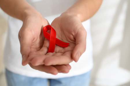 Woman holding red awareness ribbon on light background, closeup with space for text. World AIDS...