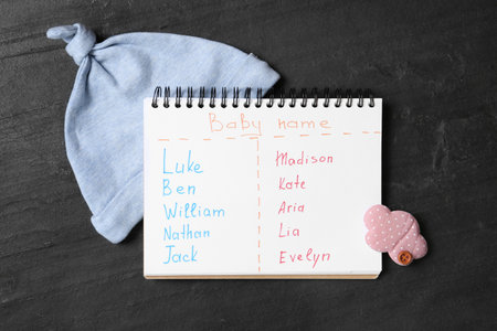 Notebook with written different baby names and child's accessories on black table, flat layの写真素材