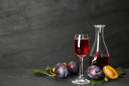 Delicious plum liquor and ripe fruits on black table. Homemade strong alcoholic beverageの写真素材