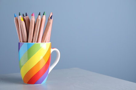 Colorful pencils in cup on grey table against light blue background. Space for textの写真素材