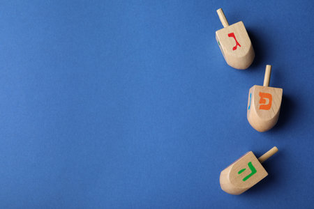 Hanukkah traditional dreidels with letters Gimel, Pe and He on blue background, flat lay. Space for textの写真素材