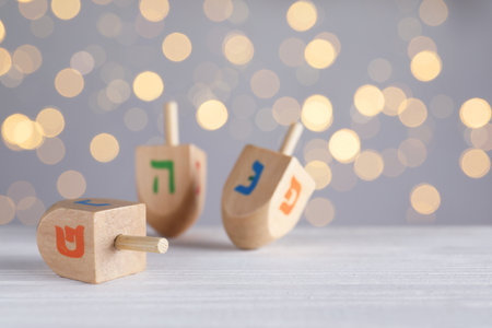 Hanukkah traditional dreidels on white wooden table against blurred lights. Space for textの写真素材