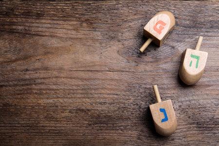 Hanukkah traditional dreidels with letters He, Pe and Nun on wooden table, flat lay. Space for textの写真素材
