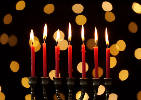Golden menorah with burning candles against dark background and blurred festive lightsの写真素材