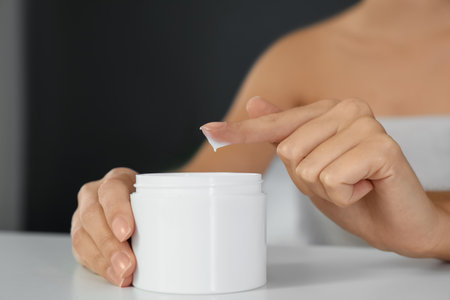 Woman with jar of moisturizing cream on white table, closeupの写真素材