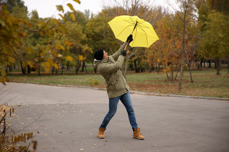 Man with yellow umbrella caught in the thick of wind outdoorsの写真素材