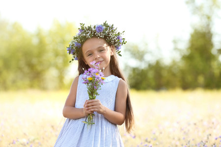 Cute little girl wearing beautiful wreath with bouquet of wildflowers outdoors. child spending time in natureの写真素材