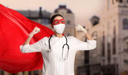 Doctor dressed as superhero on city background. Medical workers fighting dangerous diseasesの写真素材