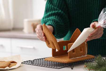 Woman making gingerbread house at white table, closeup
