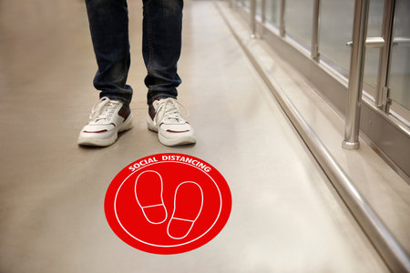 Keep social distance as a preventive measure during coronavirus outbreak. Red warning sign on floor in front of man, closeupの写真素材