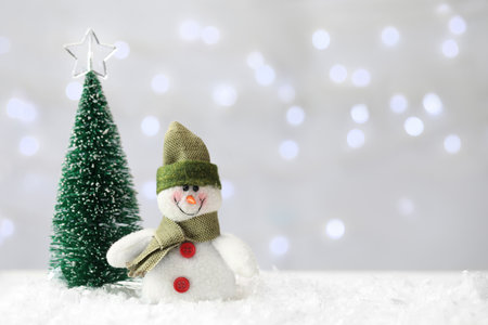 Snowman toy and Christmas tree on snow against blurred festive lights. Space for textの写真素材