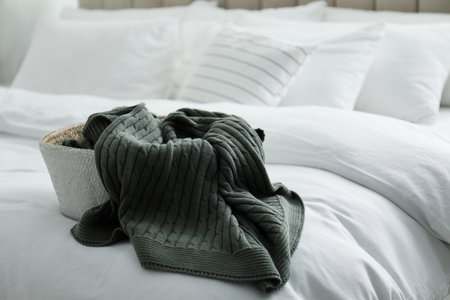 Basket with warm knitted plaid on bed indoors