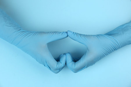 Person in medical gloves making heart with hands on light blue background, top viewの写真素材
