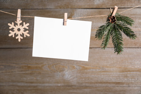Blank Christmas card and festive decor on rope against wooden background. Space for textの写真素材