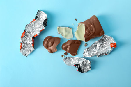 Broken chocolate Santa Claus and foil wrapper on light blue background, flat layの写真素材