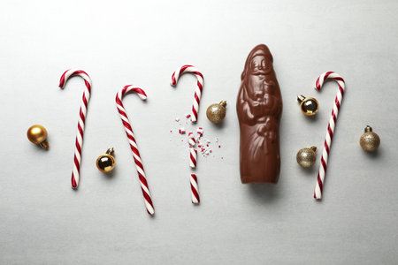 Flat lay composition with chocolate Santa Claus, candy canes and Christmas balls on light gray backgroundの写真素材