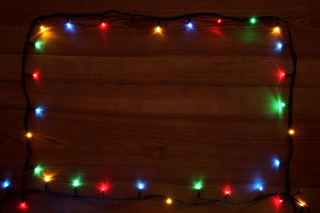 Frame of colorful Christmas lights on wooden table, top view. Space for textの写真素材