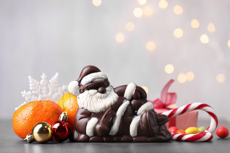 Composition with chocolate Santa Claus, sweets, tangerine and Christmas decorations on light backgroundの写真素材