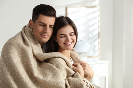 Happy couple covered with warm beige plaid indoorsの写真素材